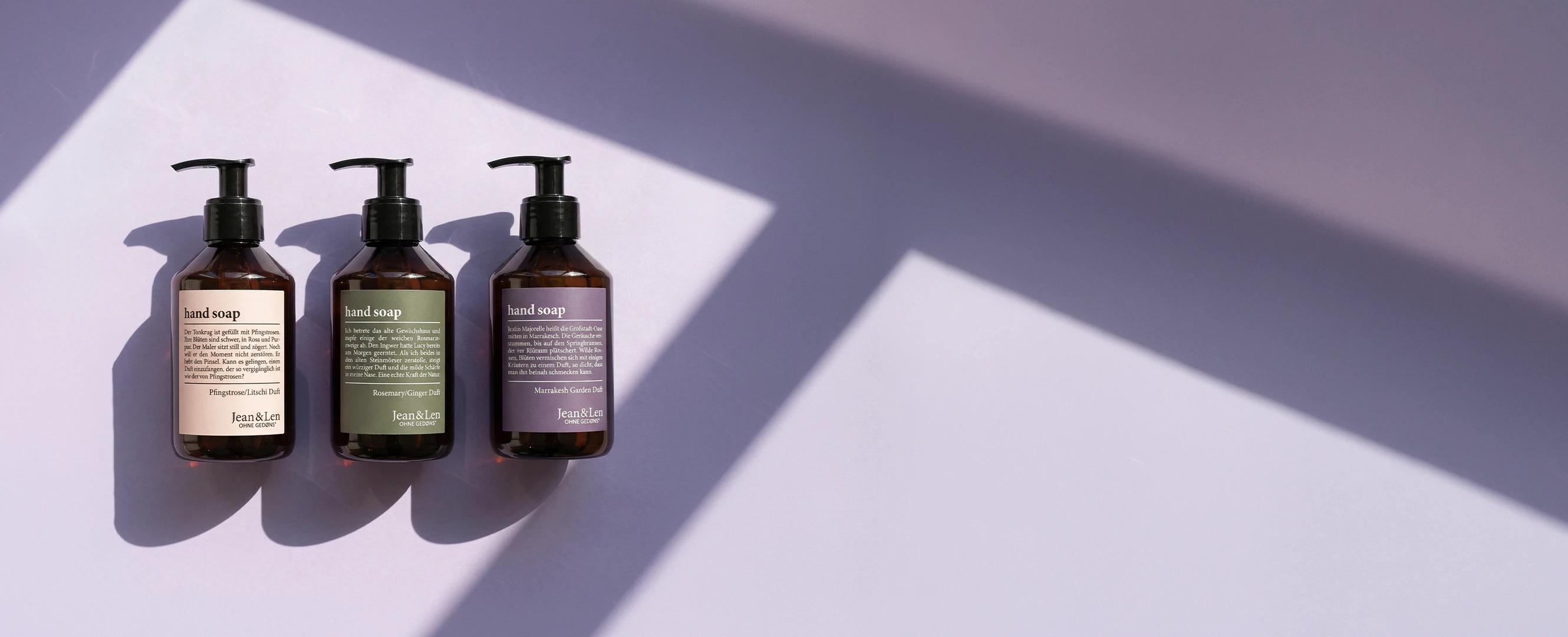 Drei Jean&Len Handseifen in braunen Pumpspendern mit unterschiedlichen Duftvarianten auf hellem Hintergrund im Sonnenlicht.