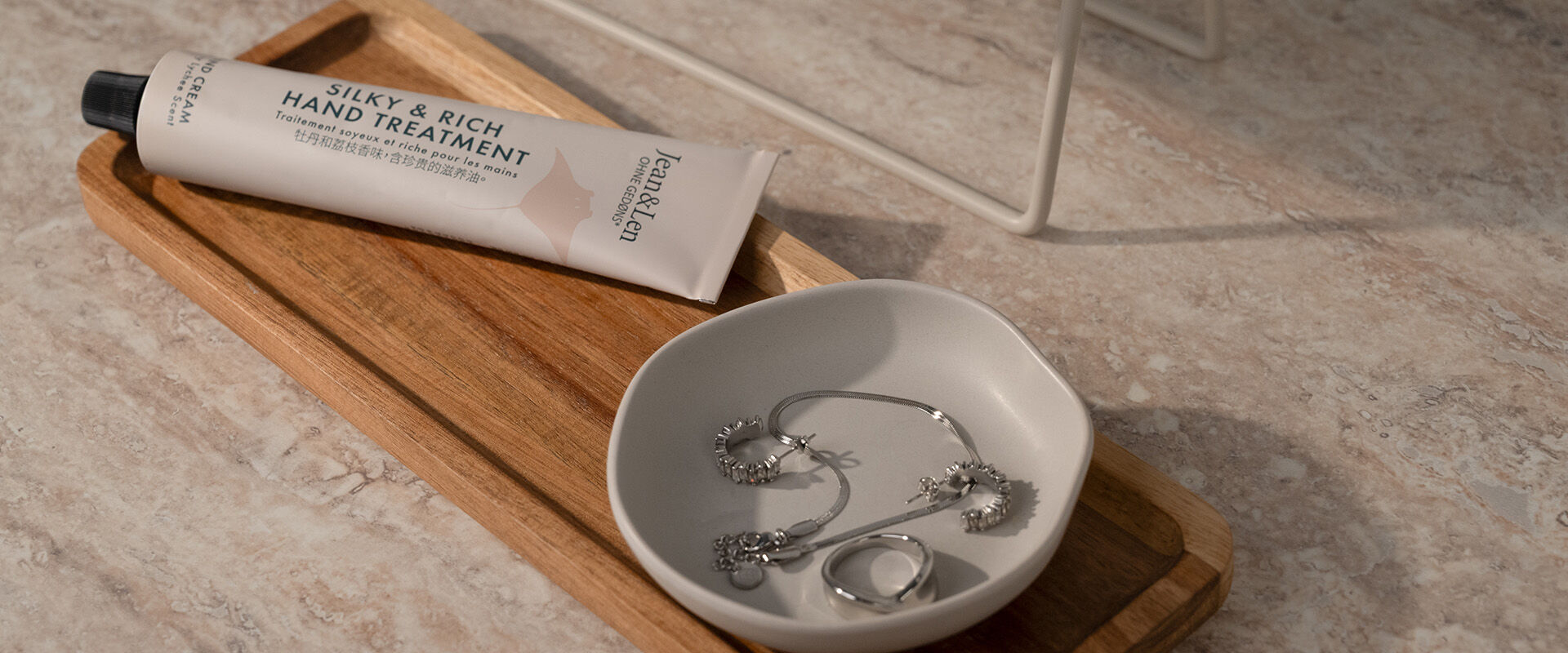 Schmuckschale mit Silberring, Kette und Ohrringen auf einem Holztablett; daneben eine Handcreme und ein Spiegel.