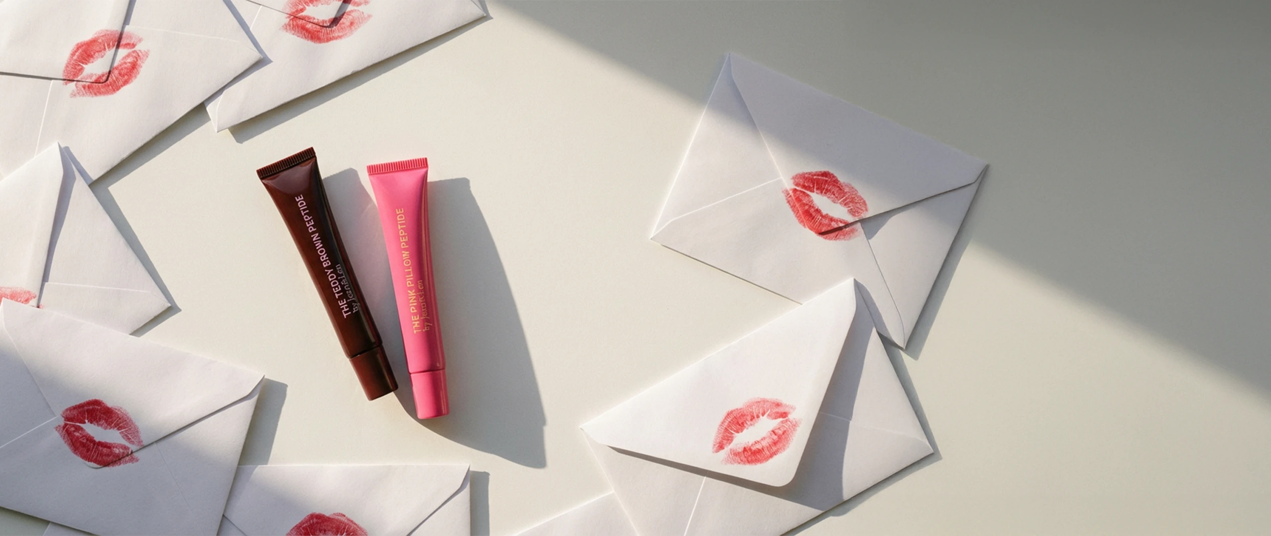 Lip Treatments Teddy Brown und Pink Pillow umgeben von Liebesbriefen mit Kuss-Abdrücken darauf.