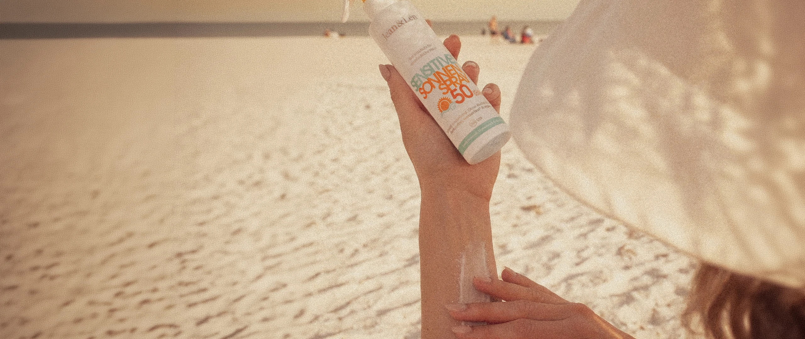 Frau trägt Jean&Len Sensitiv Sonnenspray LSF 50 am Strand auf den Arm auf.