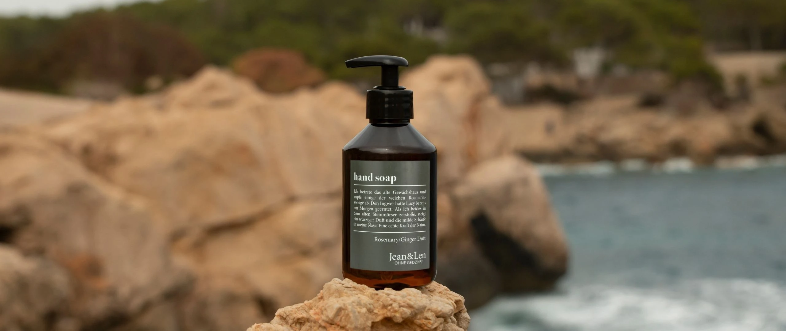 Jean&Len Handseife Rosemary/Ginger, braune Pumpflasche auf Felsen am Meer.