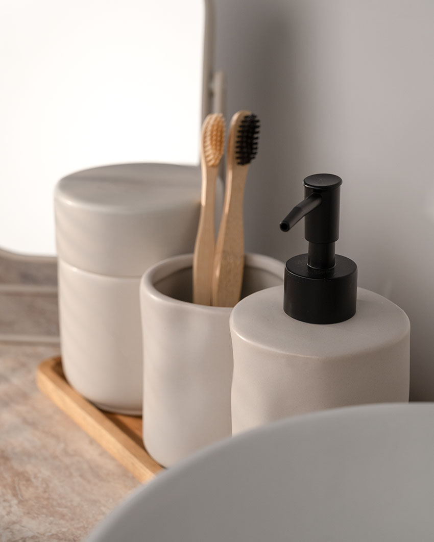 Badezimmer-Set aus Steingut mit Seifenspender, Zahnbürstenhalter und Dose auf einem Holztablett vor einem Spiegel.