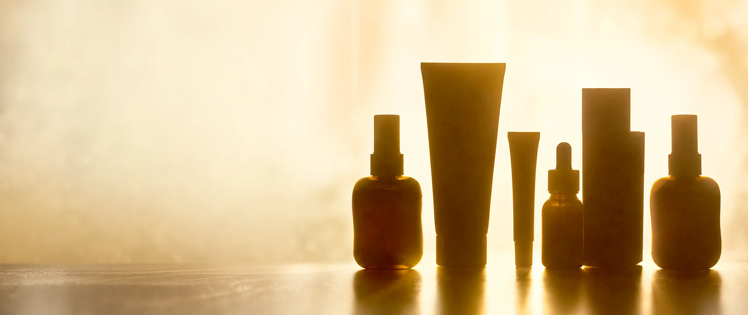 Silhouetten von verschiedenen Kosmetikprodukten vor einem sonnigen Hintergrund.