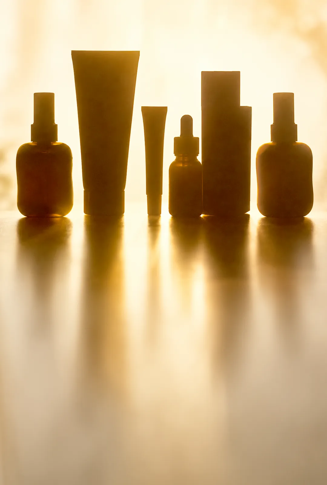 Silhouetten von verschiedenen Kosmetikprodukten vor einem sonnigen Hintergrund.