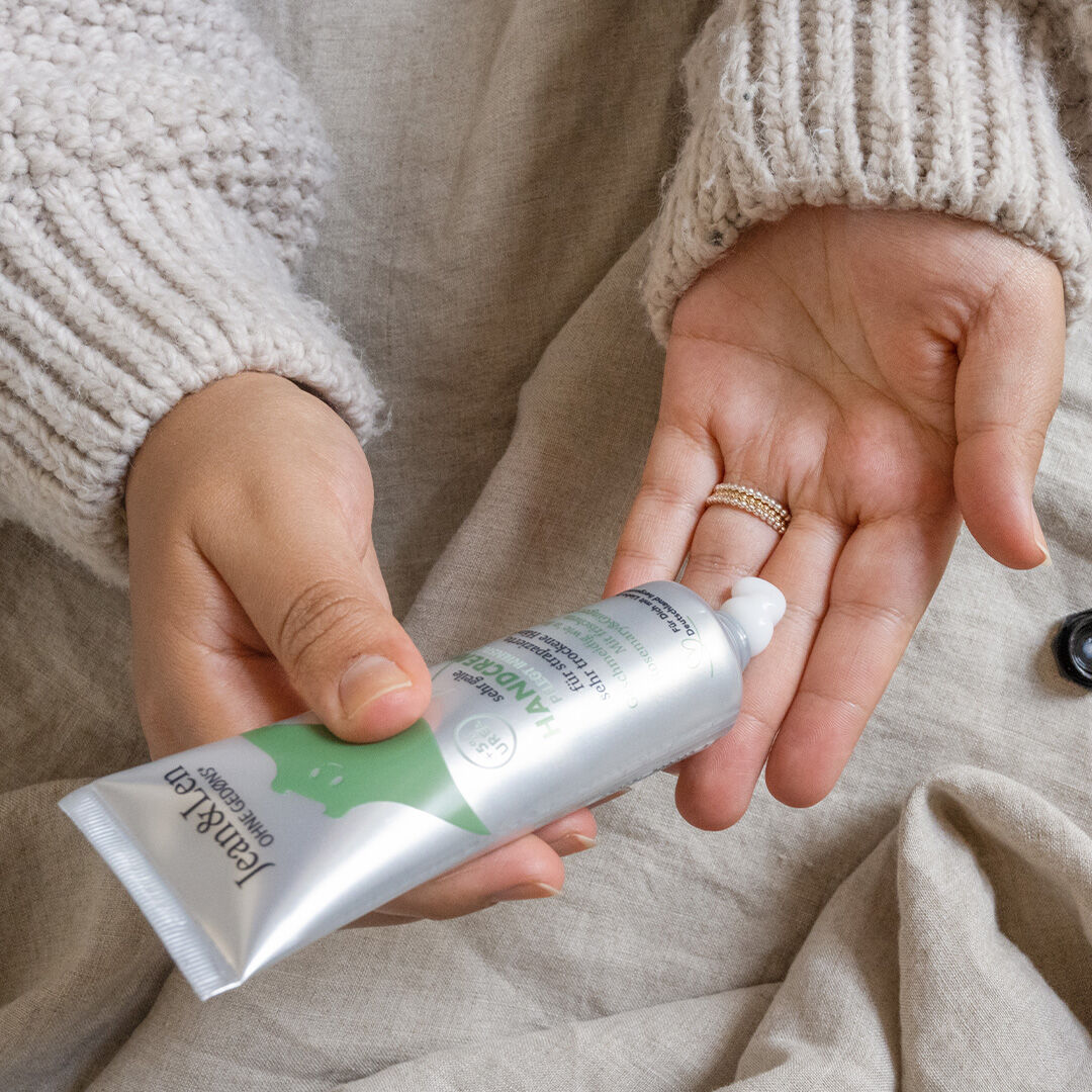 Sanfte Handpflege mit Jean&Len Handcreme – ideal für raue und trockene Hände Person mit Strickpullover trägt Jean&Len Handcreme aus Alutube auf die Hand auf